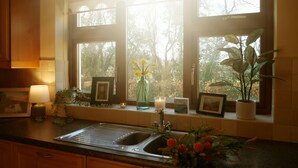 Eine Küche mit Fensterbank, die mit Blumen geschmückt ist, einem Spülbecken und Holzschränken.