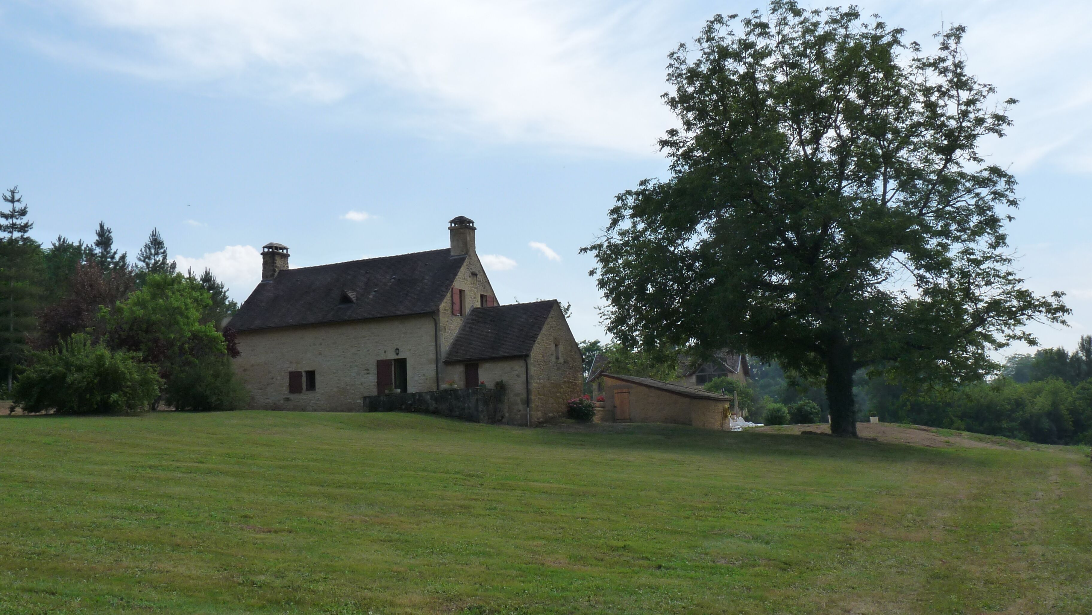 Ein Haus aus Stein mit einem geneigten Dach, einem Schornstein und einem kleinen Anbau.