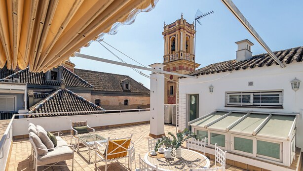 Una terraza en la azotea con mobiliario exterior, vista a un edificio histórico y un invernadero.