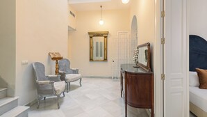 Un pasillo espacioso con techo alto, una escalera y una zona de estar con sillas y una mesa.