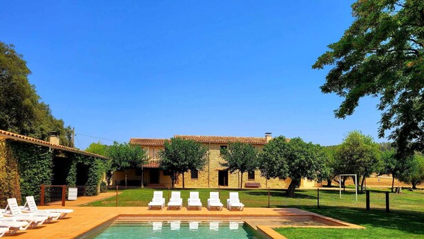 A rectangular swimming pool with a tiled edge, surrounded by a grassy area and a stone building with a tiled roof. - Rural house in Girona. 11 bedrooms, up to 30 people, private pool. (Cabanelles)
