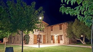 A stone building with a central courtyard, surrounded by trees and illuminated by street lamps. - Rural house in Girona. 11 bedrooms, up to 30 people, private pool. (Cabanelles)