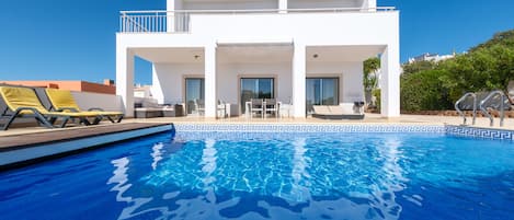 A modern two-story house with a swimming pool, outdoor furniture, and a balcony.