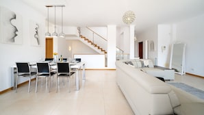A modern living room with a white sofa, dining table with chairs, and a staircase leading to an upper level. - Spacious villa near town [46] (Lagos)