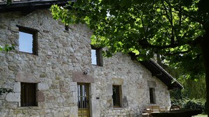 A stone building with multiple windows and a door, surrounded by greenery and a stone bench. - Etxetxobarri, a single-family farmhouse with views of the Anboto mountain range. (Mallabia - bizkaia)
