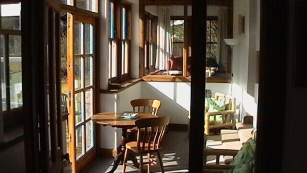 A room with a wooden table and chairs, large windows, and a view of the outdoors.