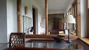 A room with a glass-top table, a wooden chair, a lamp, and a mirror reflecting a door and a window.