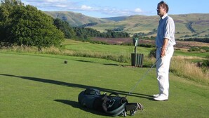 A golf course with a person standing next to a bag and golf clubs.