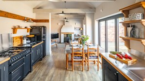 A modern kitchen with a central island, wooden beams, and large windows. - The Old Butcher's Stores, Heacham, Norfolk (Heacham)