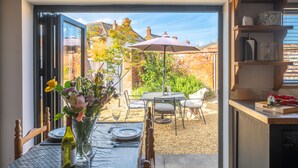 An open-plan living space with a dining area, a view of the garden, and a kitchen area. - The Old Butcher's Stores, Heacham, Norfolk (Heacham)