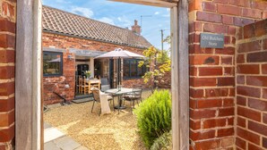 A brick building with a tiled roof, a patio area with outdoor furniture, and a sign reading "Old Butchers Store". - The Old Butcher's Stores, Heacham, Norfolk (Heacham)