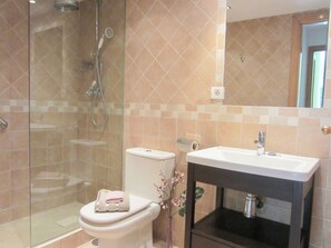 Un baño con ducha envuelta en vidrio, inodoro y lavamanos con mueble oscuro.