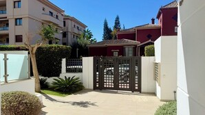 Una entrada cerrada a una zona residencial con camino de entrada pavimentado, un árbol pequeño y un seto.