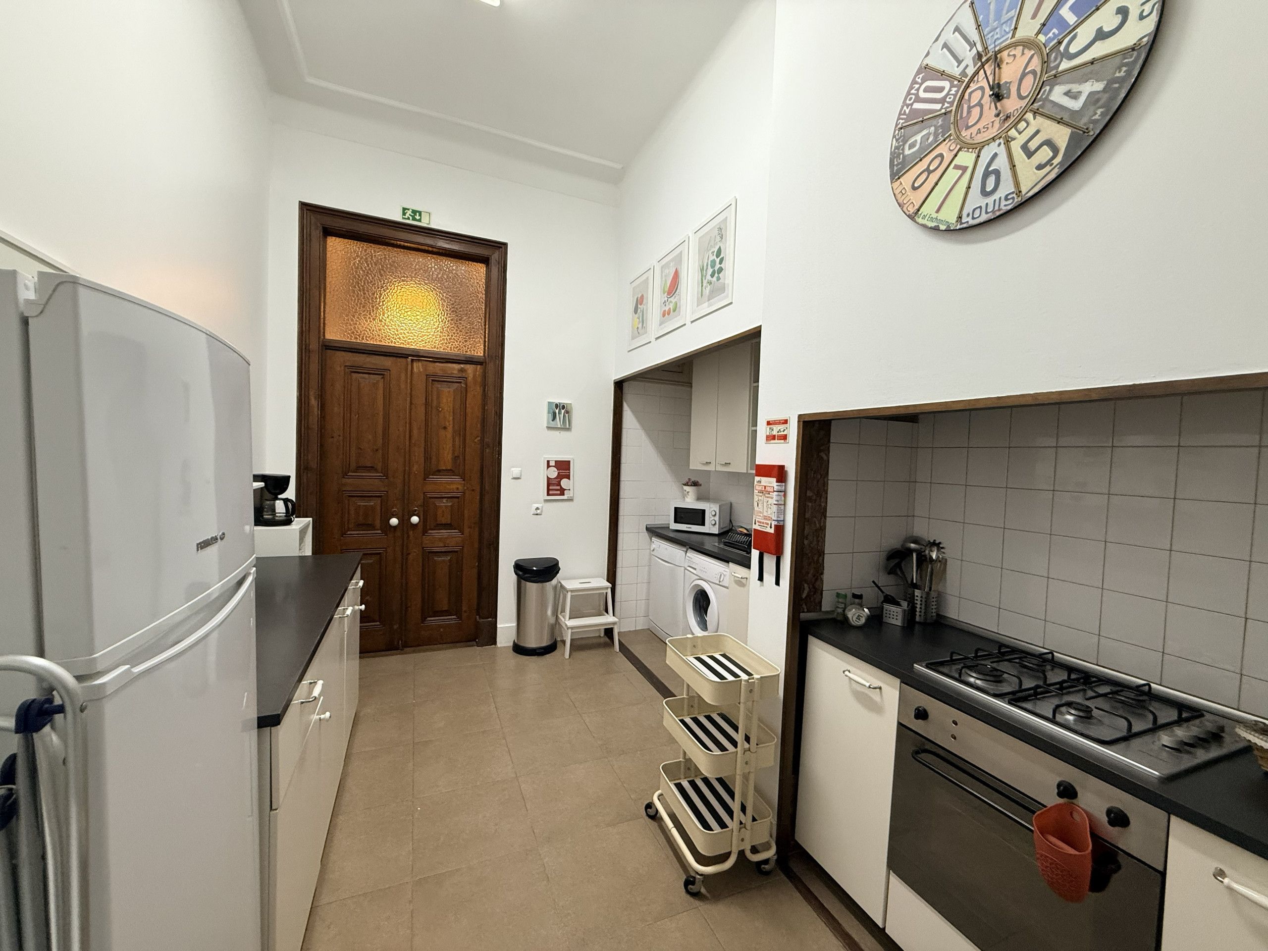 Een keuken met een koelkast, fornuis, magnetron en een wandklok.