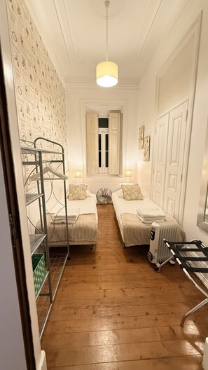 A hotel room with two beds, a radiator, a standing heater, a ceiling light, and a wall with a patterned design.
