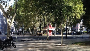 A tiled pavement with a decorative pattern, trees, and a red kiosk in the background.