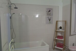 A bathroom with a shower, a bathtub, a toilet, and a shelf with decorative items.