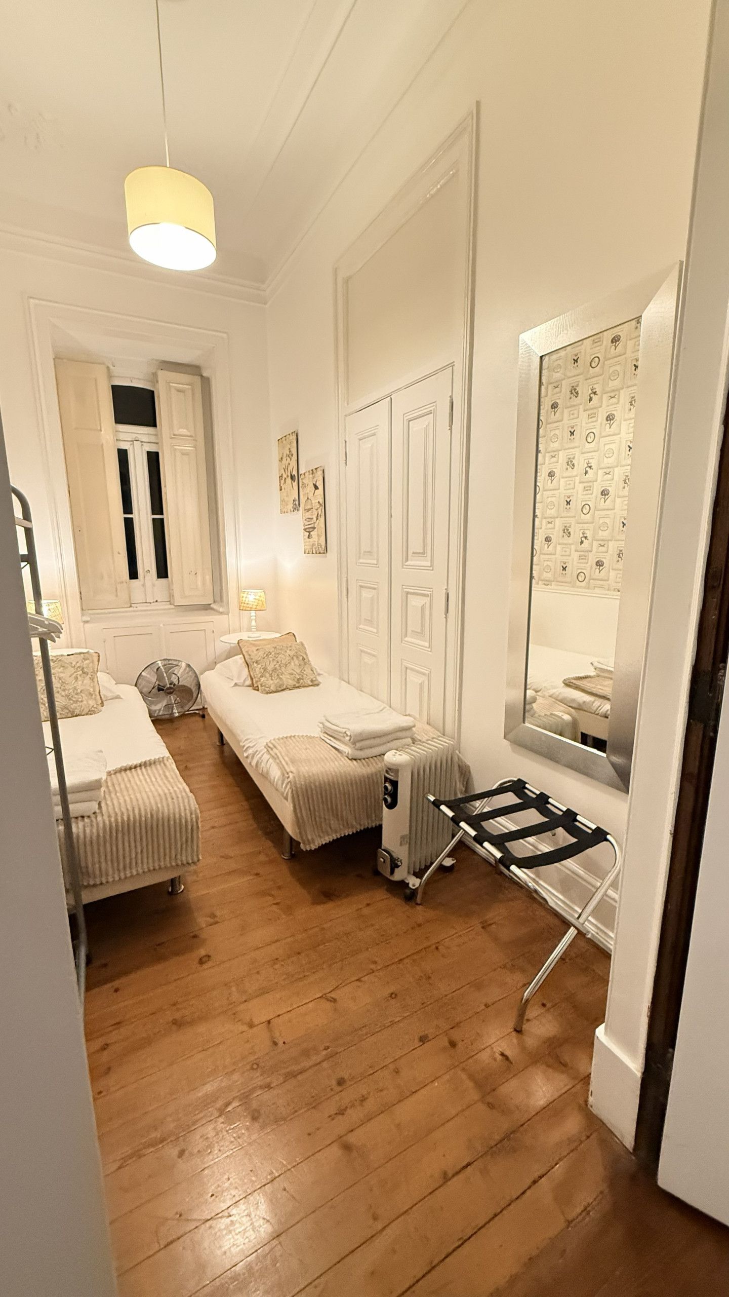 A small, well-lit bedroom with a single bed, a radiator, and a mirror reflecting the room.