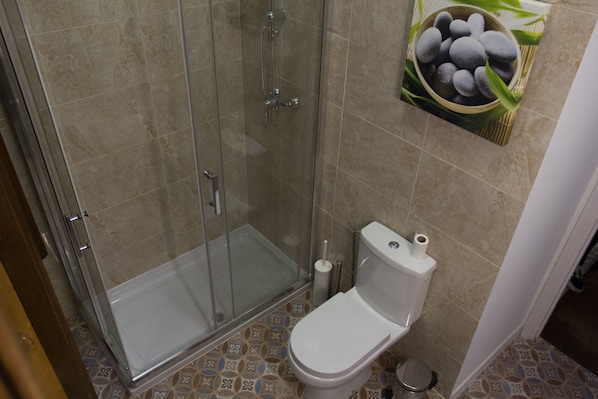 A bathroom with a glass-enclosed shower, a toilet, and patterned floor tiles.