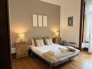 A neatly arranged bedroom with a bed, two bedside tables, a radiator, and wall art.