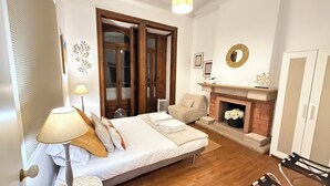 A bedroom with a bed, a lamp, a fireplace, and a wardrobe.