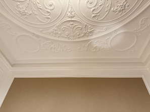 A ceiling with ornate plasterwork and a plain, beige-colored wall below.
