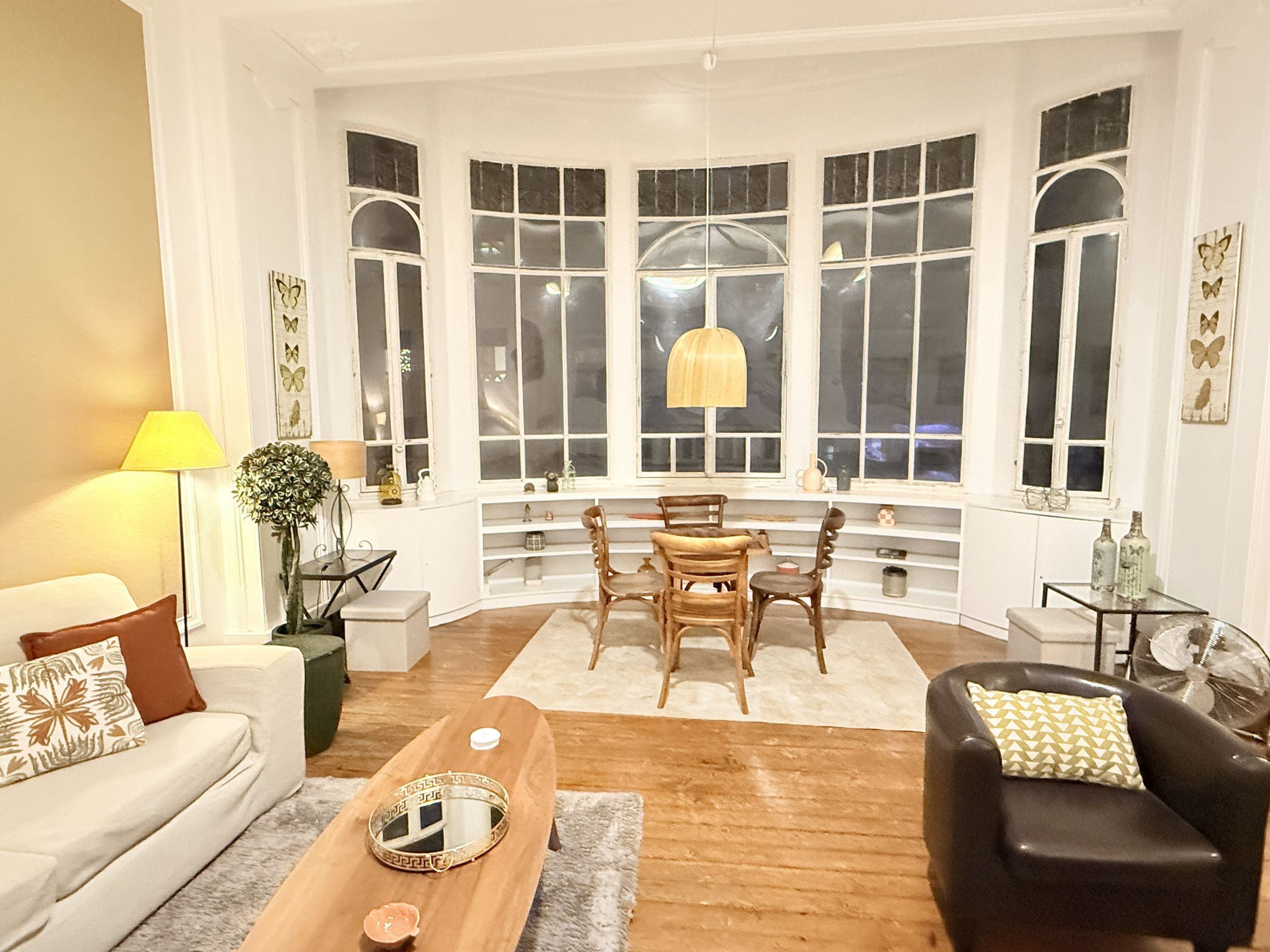 Una habitación con ventanal, una mesa de comedor con sillas, un sofá, una mesa auxiliar y una lámpara.