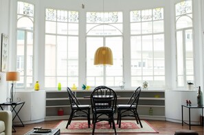 A bright room with large windows, a table with chairs, and various decorative items on the windowsill.