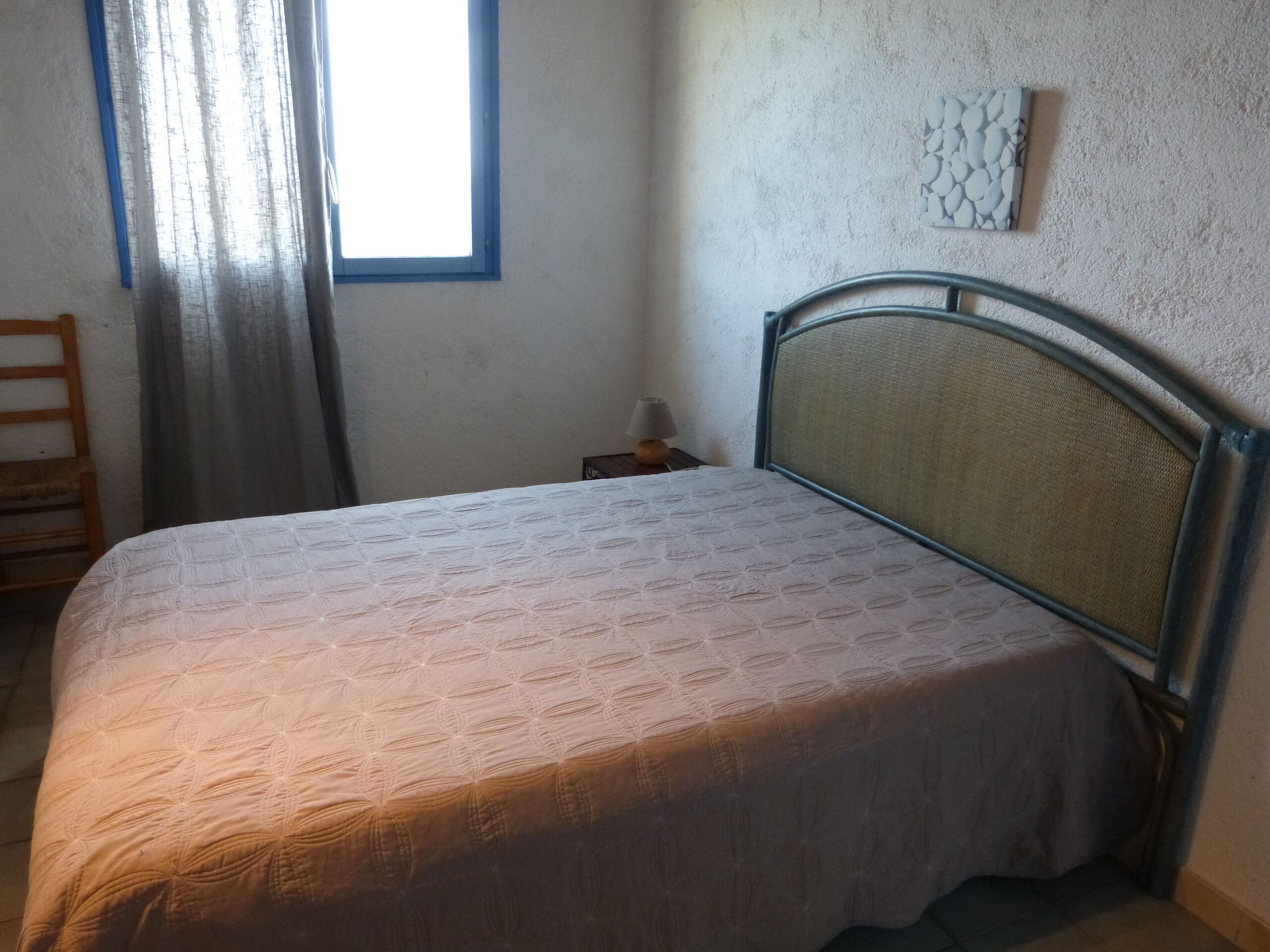Een slaapkamer met een bed, nachtkastje, lamp, raam met gordijnen en een gestructureerde wand.