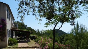 Ein Haus mit Terrasse, ein Garten mit rosa Blumen und Blick auf eine Hügelkette.
