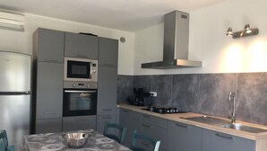 Eine moderne Küche mit grauen Schränken, einem Edelstahl-Kühlschrank, einem Backofen, einer Mikrowelle, einem Gasherd und einer Spüle.