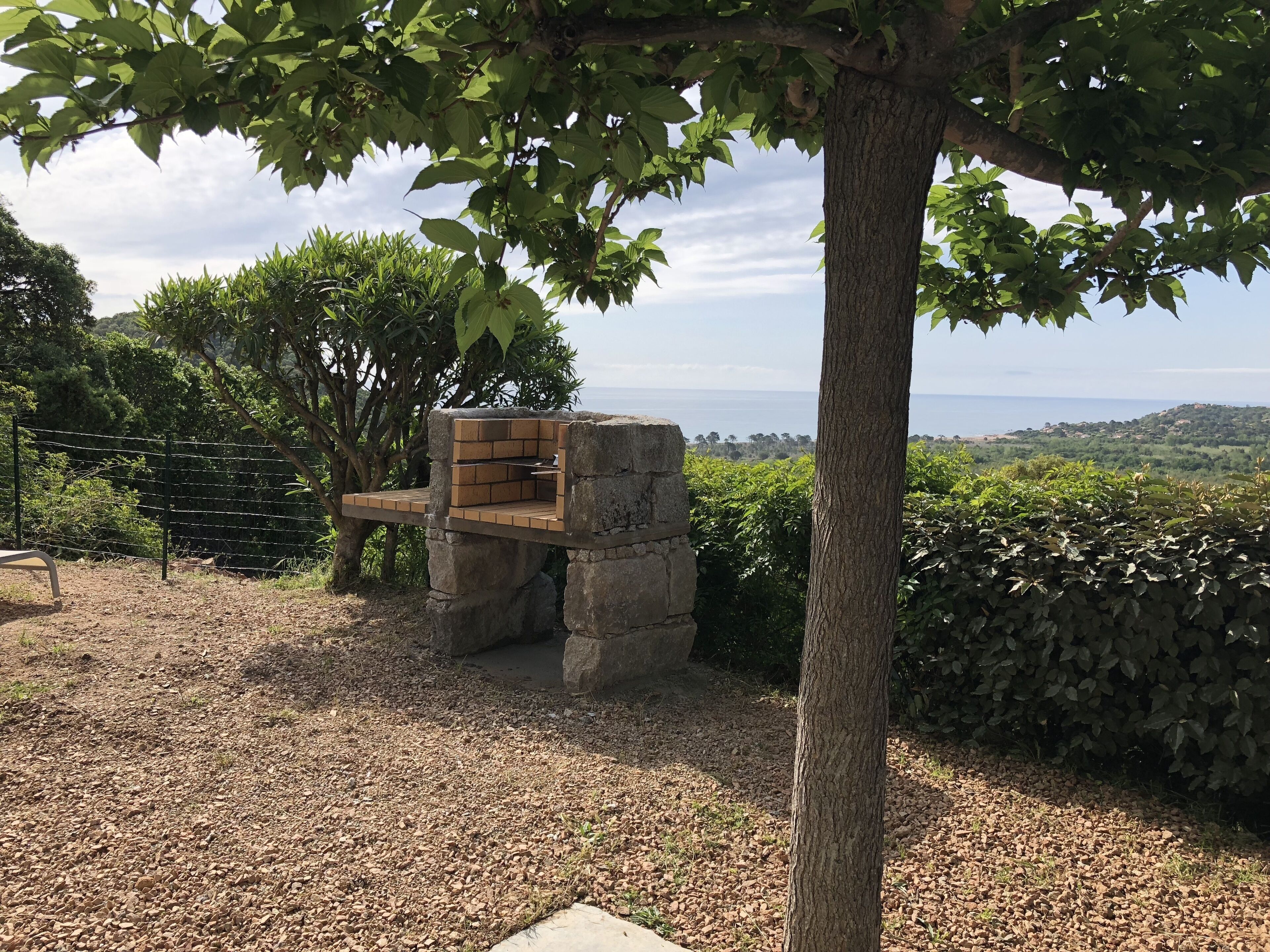 Un barbecue en pierre avec un banc, entouré d’arbres et offrant une vue sur un paysage lointain.
