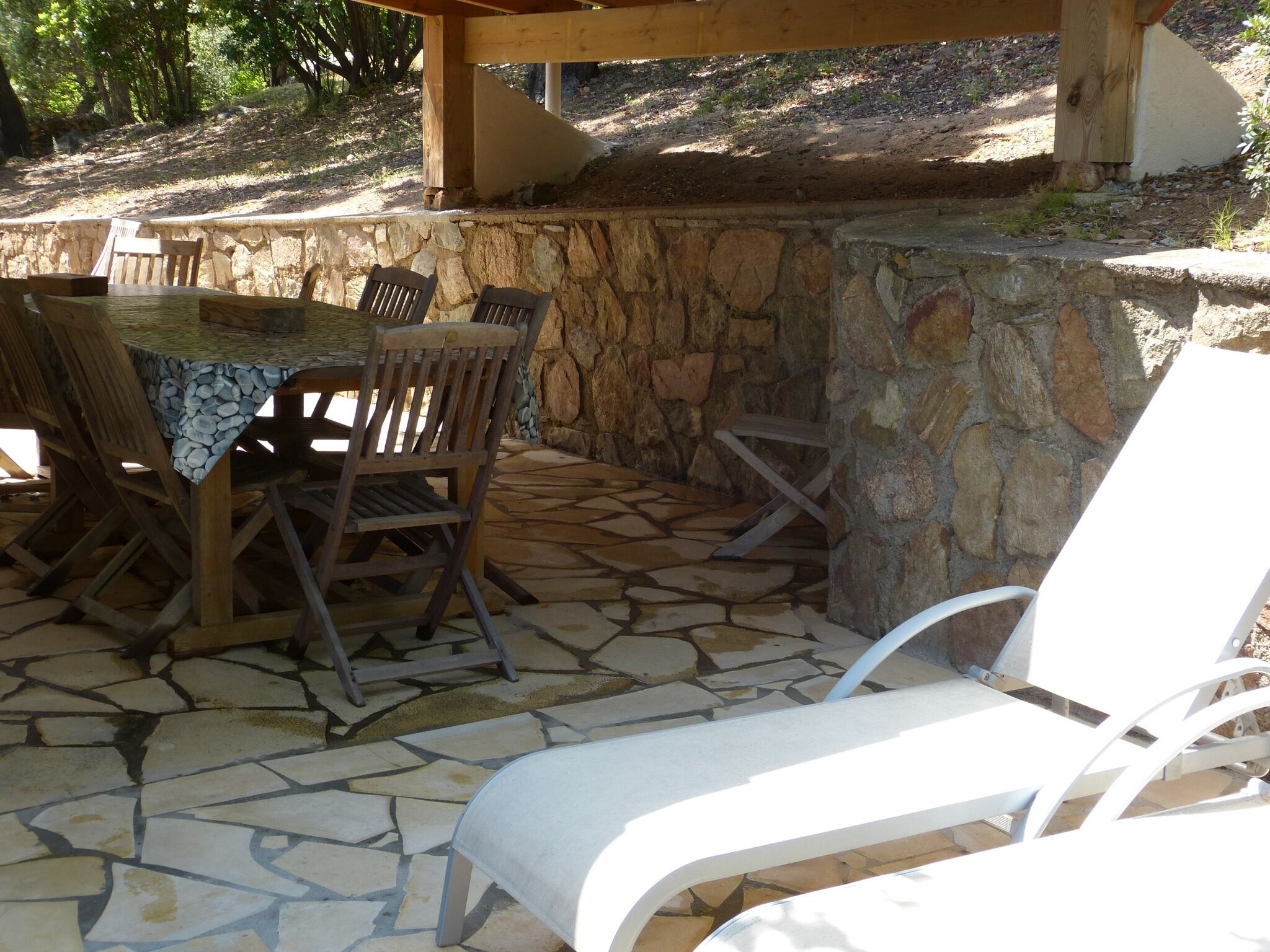 Un patio al aire libre con suelo de piedra, una mesa de madera con sillas y un muro de piedra.