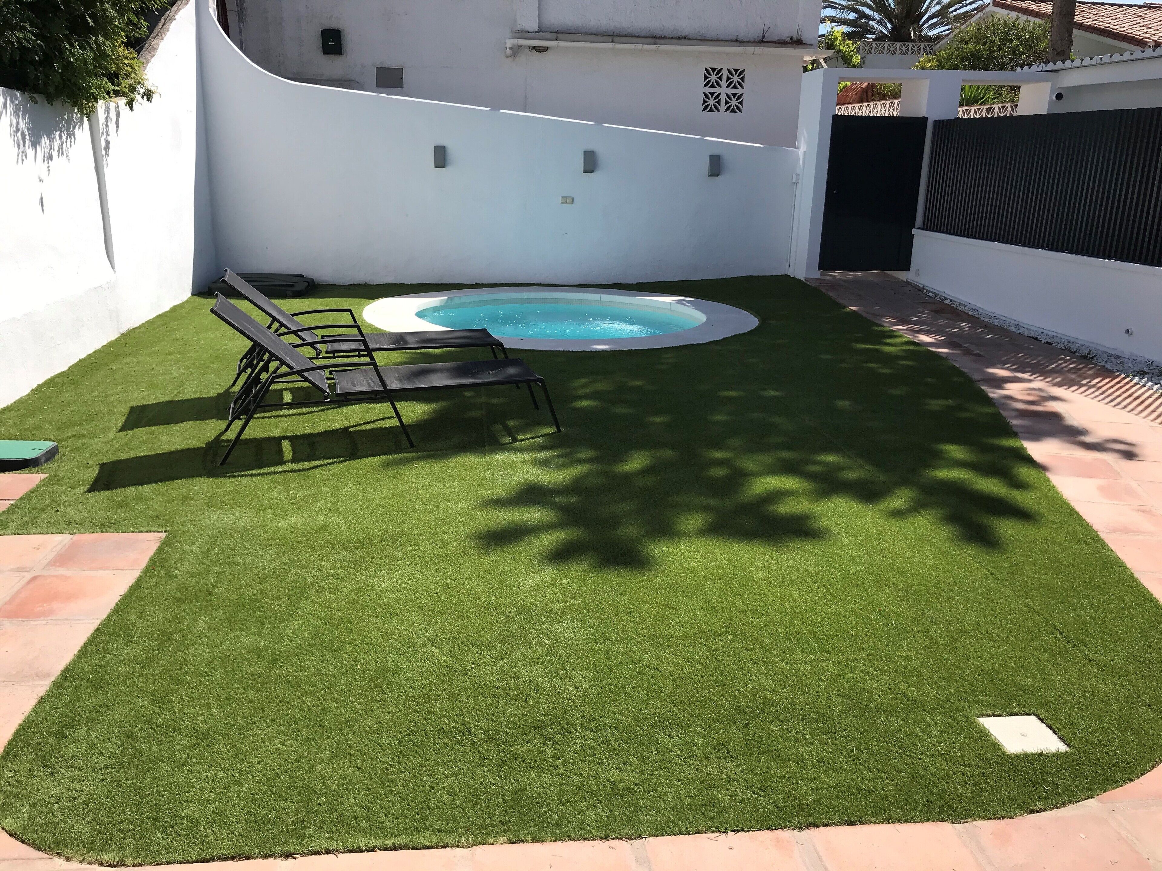 A backyard with artificial grass, a swimming pool, and a gated entrance.