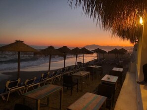Ein Restaurant direkt am Strand mit Außenbereich, einschließlich Tischen, Stühlen und reetgedeckten Sonnenschirmen.