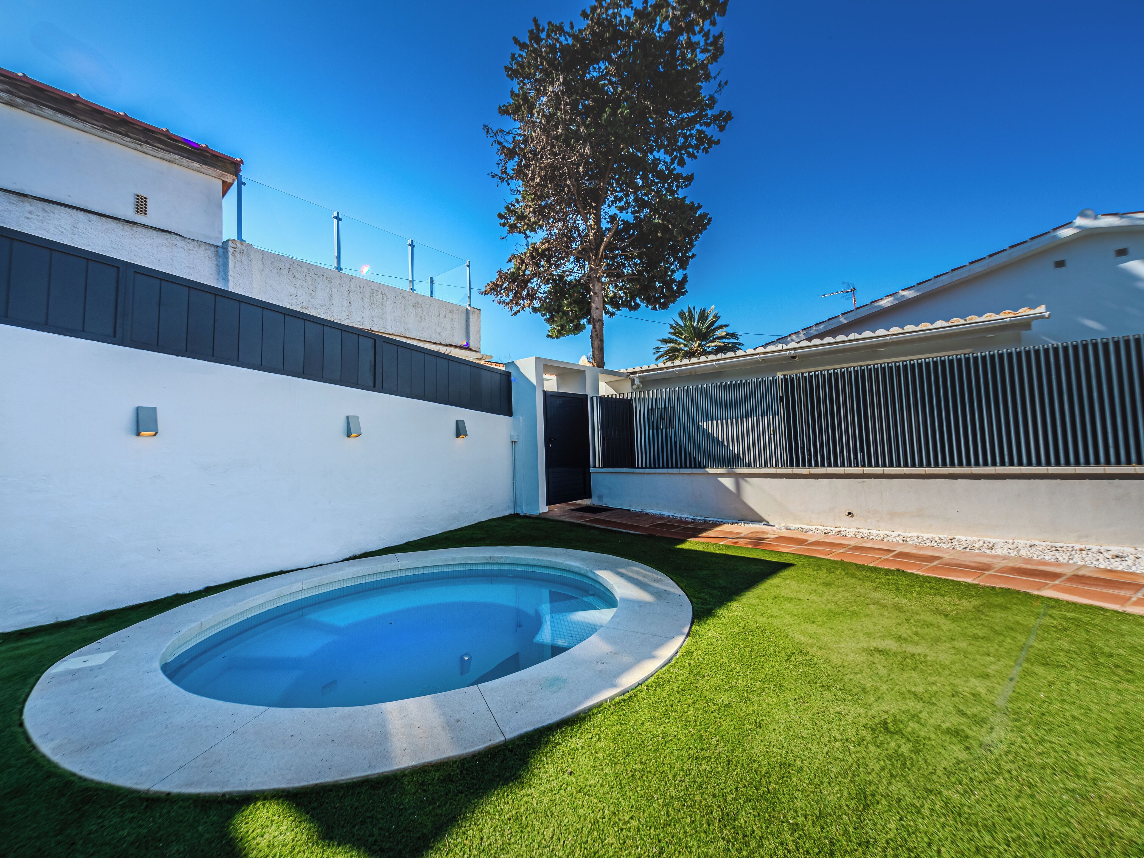 Un espace piscine extérieur moderne, doté d’une piscine circulaire, entourée d’une pelouse bien entretenue et d’un petit muret.