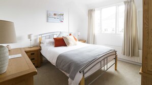Una camera da letto con un letto, comodini, una lampada, una finestra con tende, un termosifone e un quadro appeso al muro.