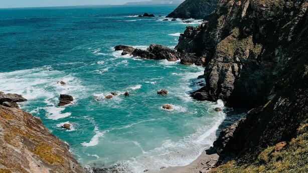 Paesaggio costiero con scogliere rocciose, una spiaggia sabbiosa e l'oceano.
