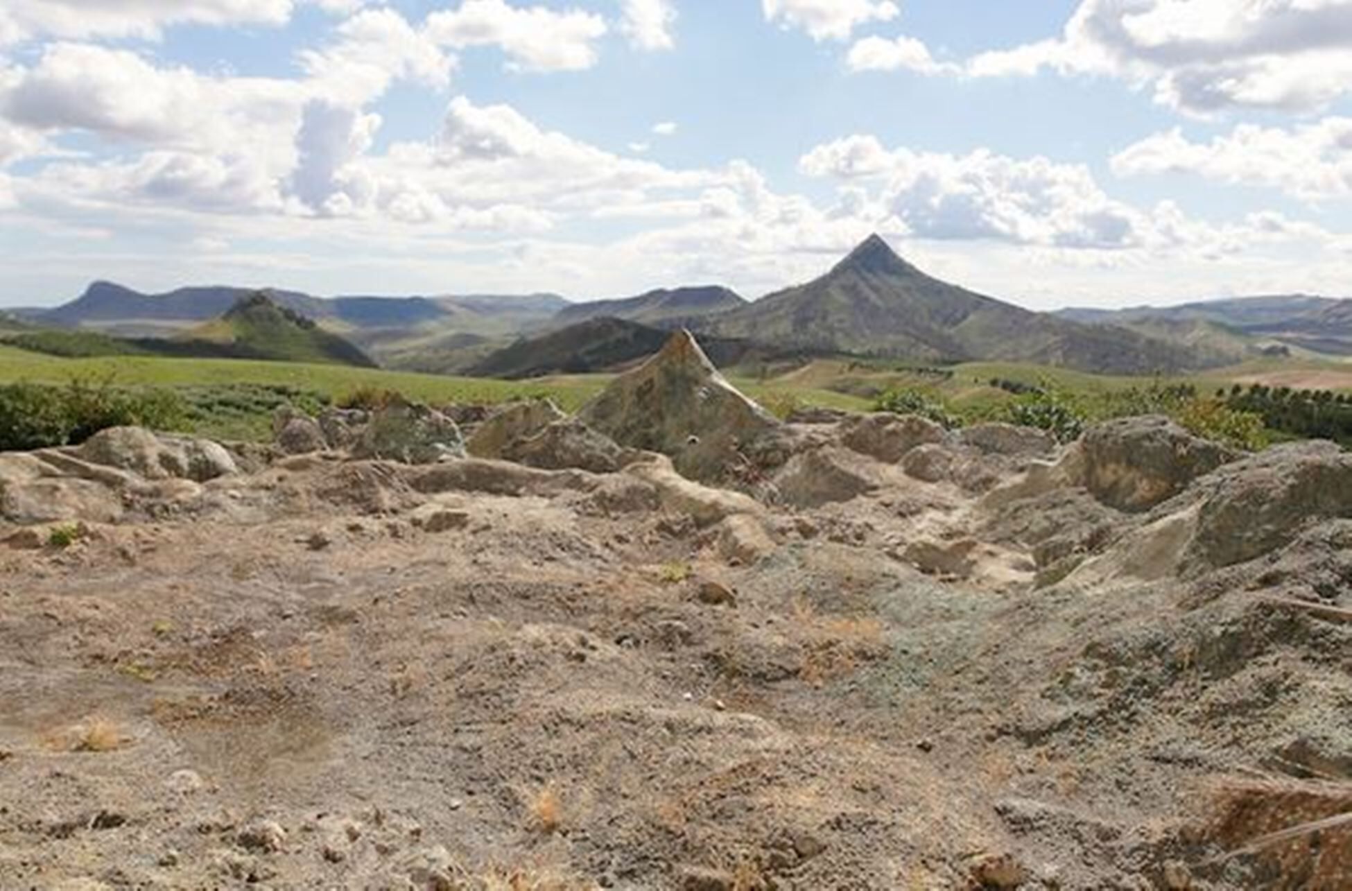 A rugged landscape with rocky terrain and distant mountains under a partly cloudy sky.