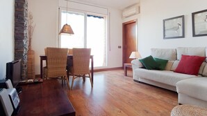 Uma sala de estar com um sofá, duas cadeiras de vime, uma mesa de madeira, uma televisão e uma parede de pedra.