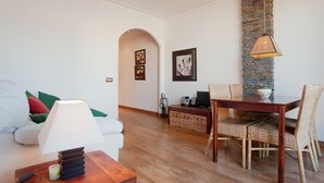Uma sala de estar com sofá, mesa de jantar com cadeiras, luminária e parede de pedra.