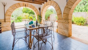An outdoor patio with a table and chairs, stone arches, and a view of greenery. - Villa Can Boseta by SunVillas Mallorca (Pollença)
