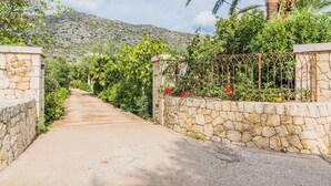 A pathway flanked by stone walls and lush greenery, leading towards a mountainous backdrop. - Villa Can Boseta by SunVillas Mallorca (Pollença)