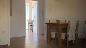 Un coin repas avec une table et des chaises en bois, un couloir menant à une autre pièce et des luminaires suspendus.