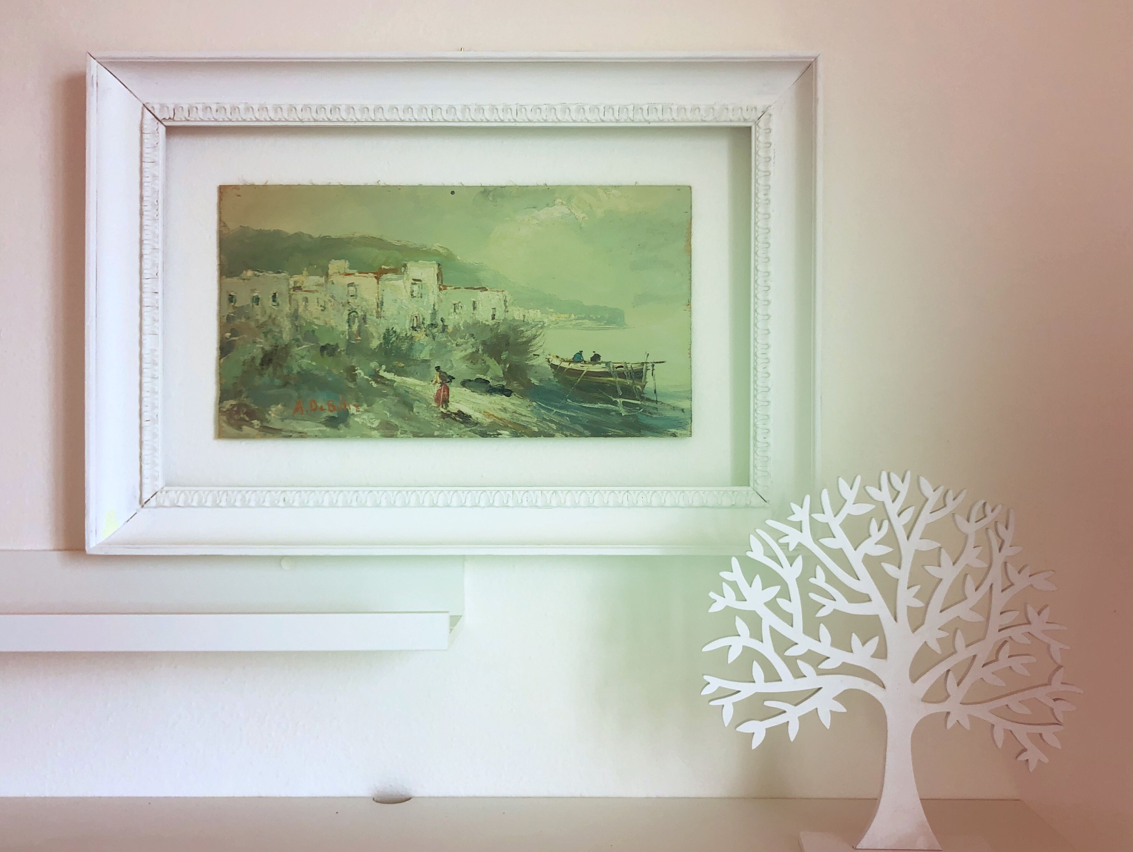 A framed painting of a coastal scene with a tree sculpture beside it.