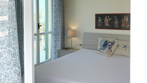 Une chambre à coucher avec un grand lit, une table de chevet avec une lampe, une fenêtre avec des rideaux et un tableau au mur.