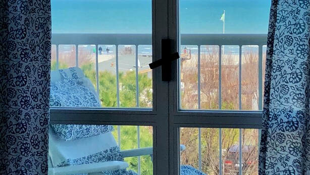 Un balcon avec vue sur la mer, une chaise blanche et une table blanche.