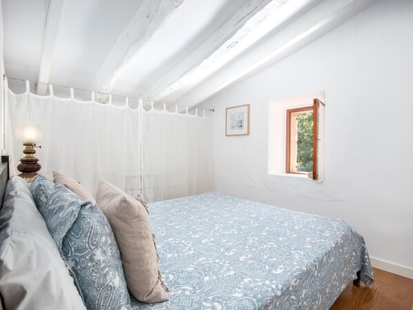 A bedroom with a bed, a bedside table with a lamp, a window, and a framed picture on the wall. - Canamon charming house with private pool. Wifi (Ses salines)