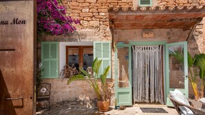 Un bâtiment rustique en pierre, doté d’une porte en bois, d’une fenêtre avec des volets verts et d’une plante en pot.