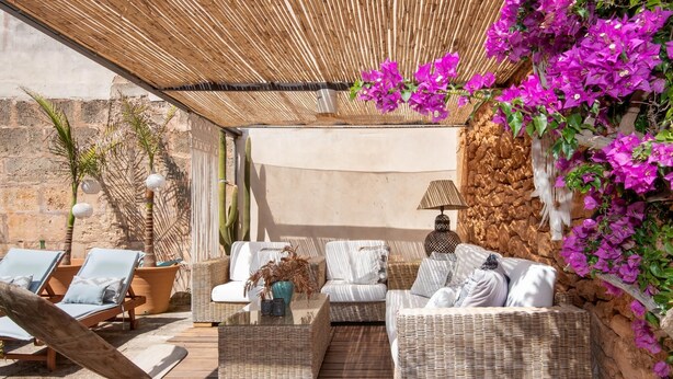 Un espace extérieur ensoleillé, aménagé avec des meubles en osier, un mur de pierre et des fleurs de bougainvillier aux couleurs vives.
